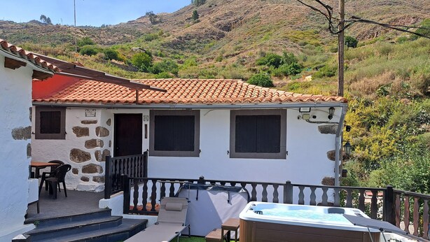 Ein Haus mit Natursteinfassade, Ziegeldach, Whirlpool und kleiner Terrasse mit Gartenmöbeln.