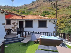 A house with a stone facade, a tiled roof, a hot tub, and a small patio with outdoor furniture.