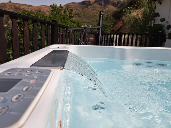 A hot tub with a control panel, surrounded by a wooden deck and a mountainous landscape.