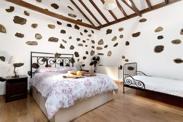 A bedroom with a stone wall, a bed with floral bedding, a nightstand with a lamp, and a bedside table with a lamp.