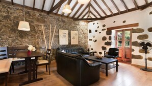 Ein Zimmer mit Steinwand, Holzbalken, einem Ledersofa, einem Esstisch mit Stühlen und hängenden Lampen.