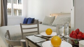 A hotel room with a bed, a dining table with plates of fruit, glasses, and a chair.