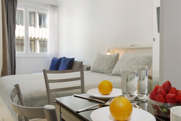Una habitación de hotel con una cama, una mesa de comedor con platos de fruta, vasos y una silla.