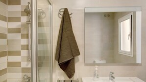 A bathroom with a glass shower enclosure, a towel rack with a towel, a sink with a soap dispenser, and a mirror.