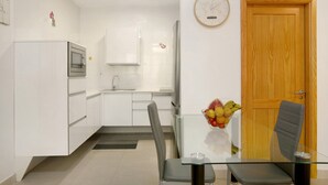 A modern kitchen with white cabinets, a microwave, and a glass dining table with a fruit bowl.