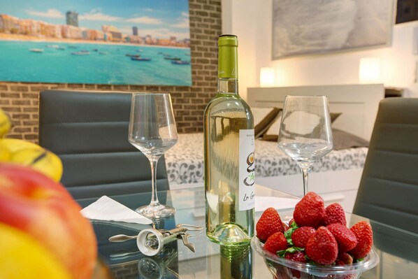 A dining table with a bottle of white wine, two glasses, a bowl of strawberries, and a key.