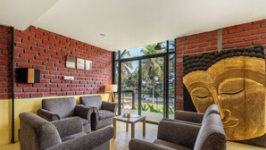 A room with a brick wall, large windows, and a golden statue. - ATMAVEDA RIVERSIDE HOMESTAY (Shrirangapattana)