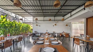 A spacious dining area with long wooden tables and chairs, a high ceiling with woven light fixtures, and large windows allowing natural light. - ATMAVEDA RIVERSIDE HOMESTAY (Shrirangapattana)