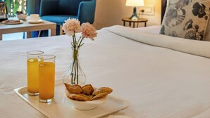 A neatly made bed with a tray of food and drinks, a vase with flowers, and a book on a bedside table. - ATMAVEDA RIVERSIDE HOMESTAY (Shrirangapattana)