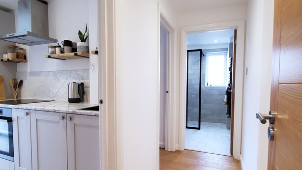 A modern kitchen with white cabinetry, a wooden countertop, and a built-in stove. A hallway with wooden flooring leads to a glass door. - Saltdean annexe, excellent location (Saltdean)