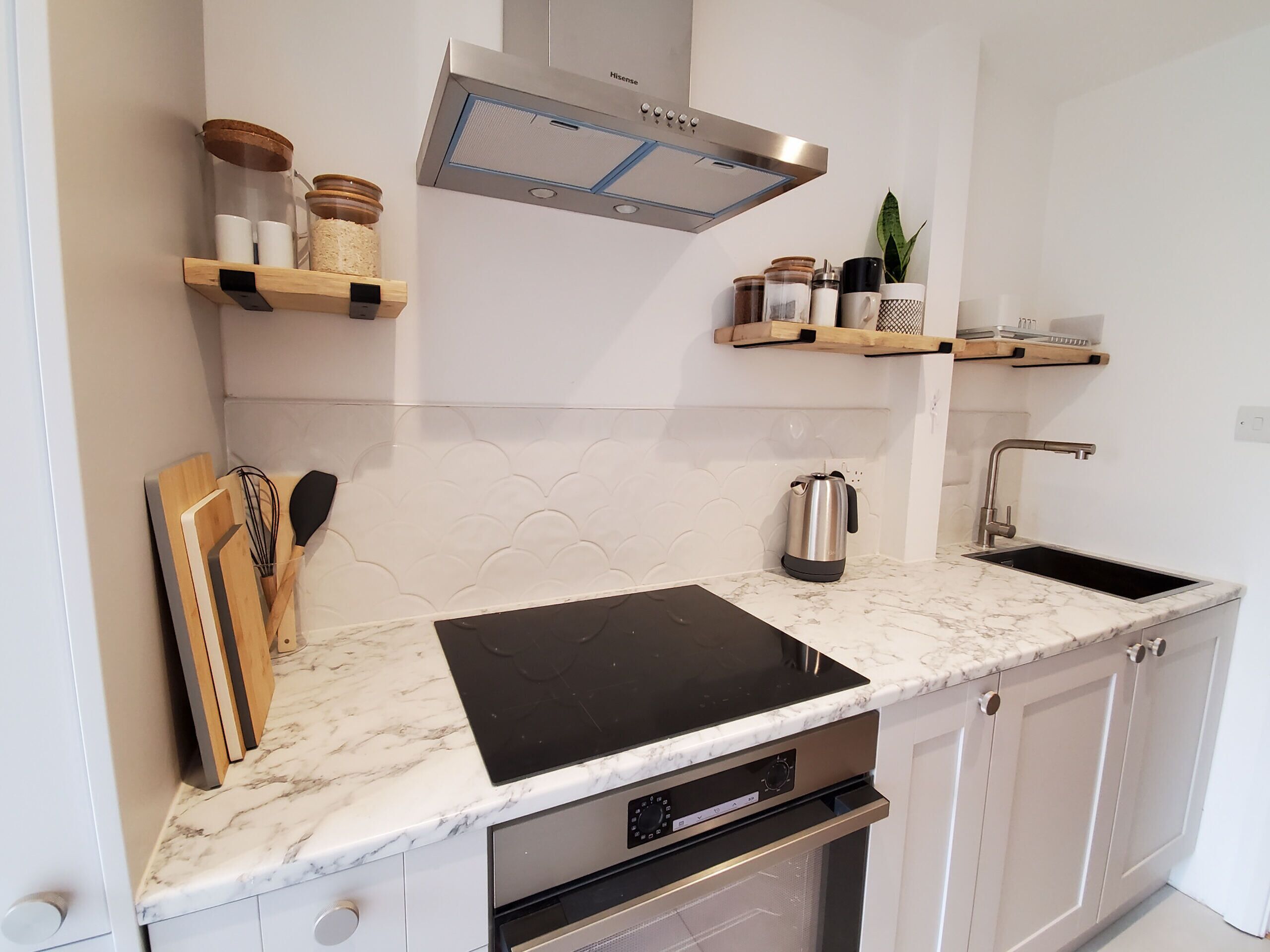 Una cocina moderna con armarios blancos, una placa de cocción por inducción negra, una campana extractora de acero inoxidable, un fregadero y un horno empotrado.