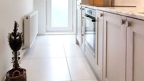 A narrow hallway with a white door at the end, a radiator on the left, and a kitchen area on the right with cabinets and a stove. - Saltdean annexe, excellent location (Saltdean)
