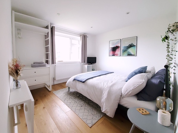 Une chambre à coucher avec un lit, un bureau, un radiateur, une télévision et des œuvres d’art accrochées au mur.