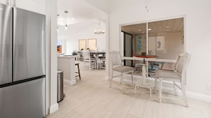Une cuisine moderne dotée d’un réfrigérateur en acier inoxydable, de meubles blancs et d’un coin repas avec une table et des chaises en bois.