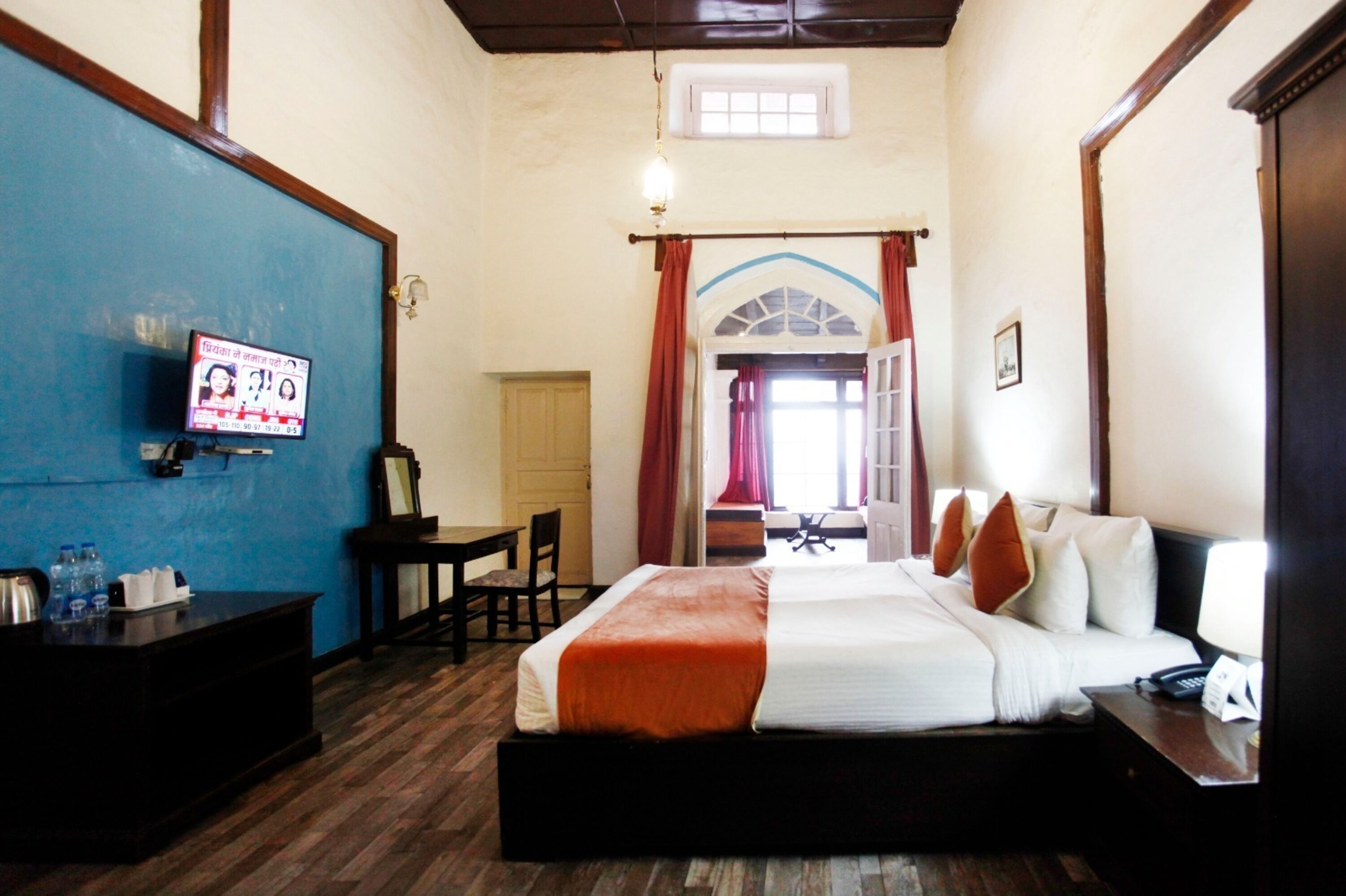 Habitación de hotel con cama, escritorio, televisión y ventana con cortinas.
