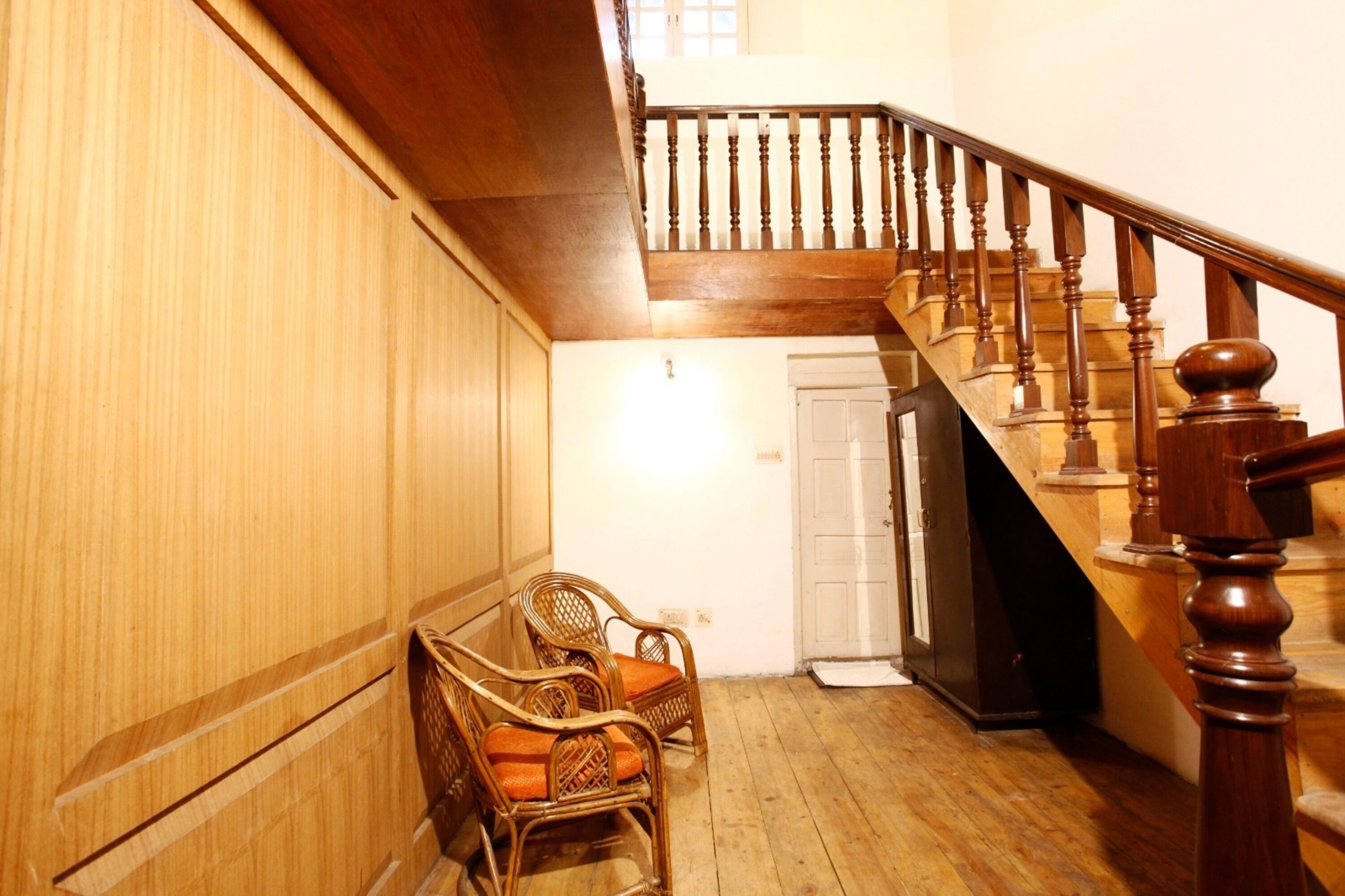 A wooden staircase with a balustrade, a door, and wicker chairs in a room with wooden flooring.