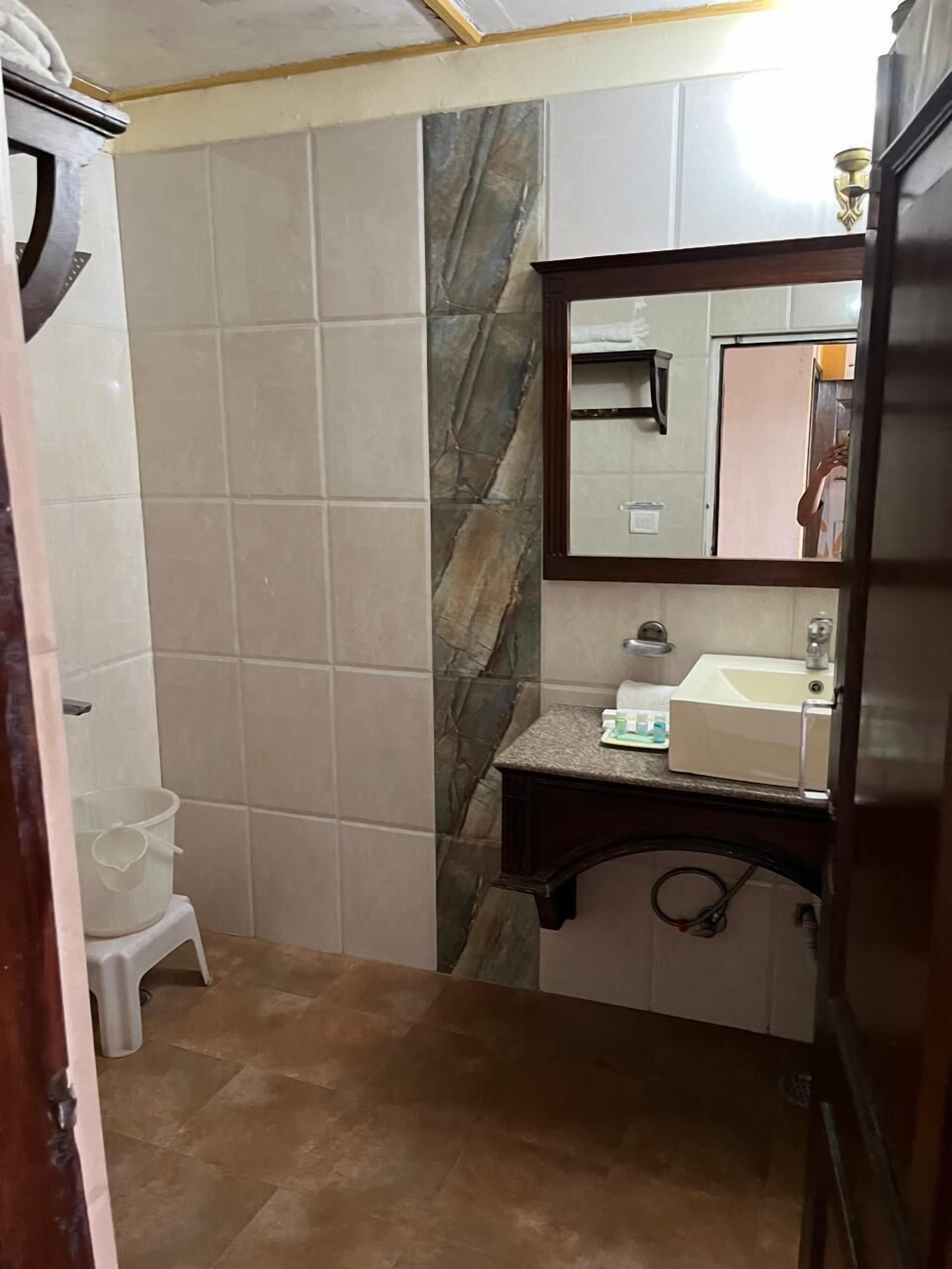 Een badkamer met betegelde vloer, een wastafel met spiegel, een klein krukje en een kast.