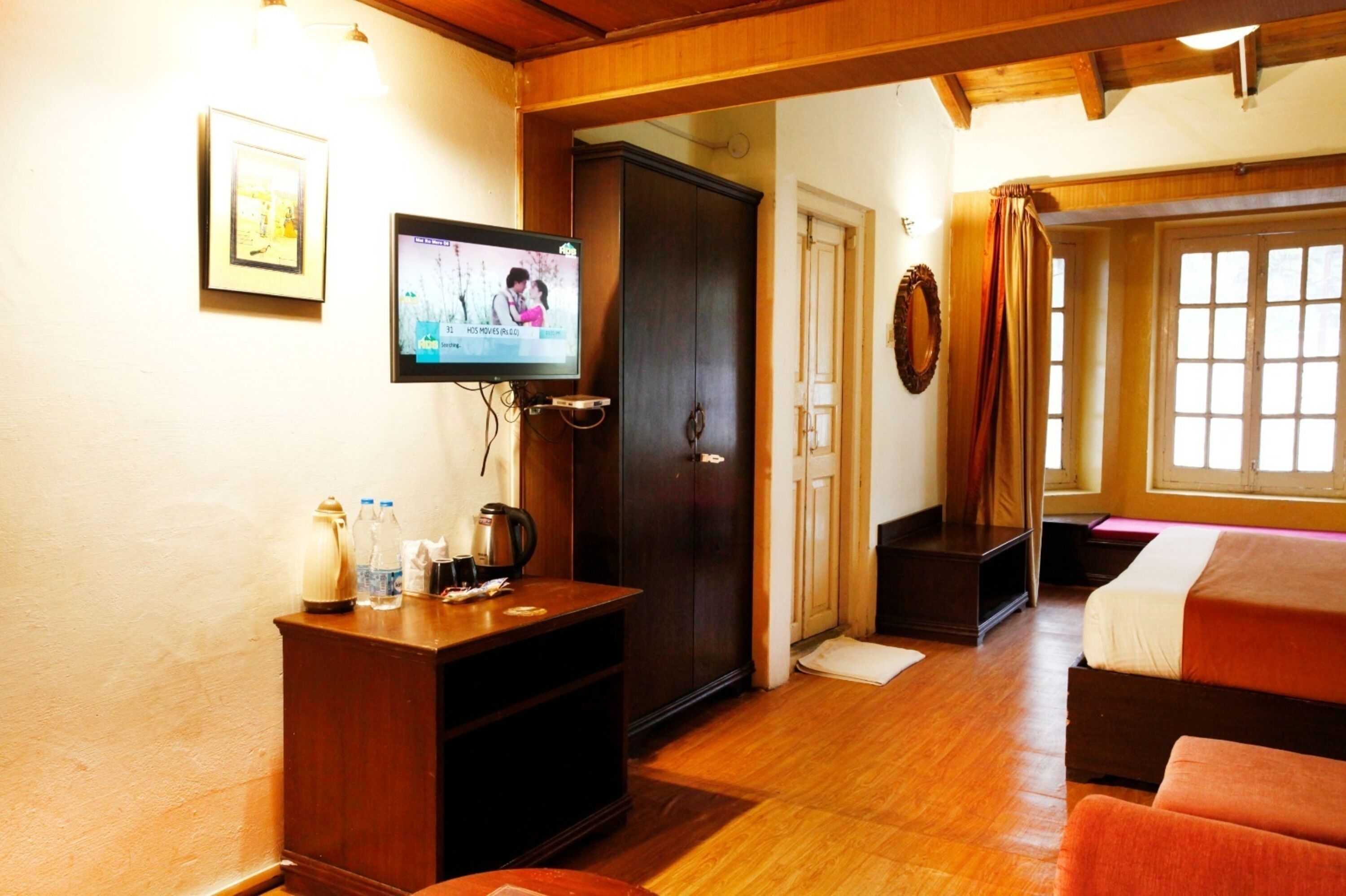 Una habitación acogedora con suelo de madera, un televisor montado en la pared, un armario y una cama con una manta roja.