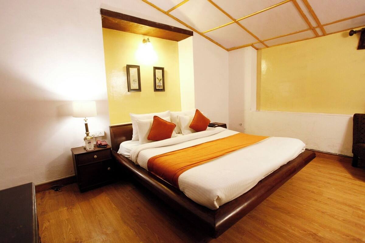 Una habitación de hotel con una cama de madera, ropa de cama blanca, una mesita de noche con lámpara y una ventana con vistas.
