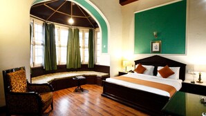 Une chambre d’hôtel avec un grand lit, un coin salon près de la fenêtre et une petite table.