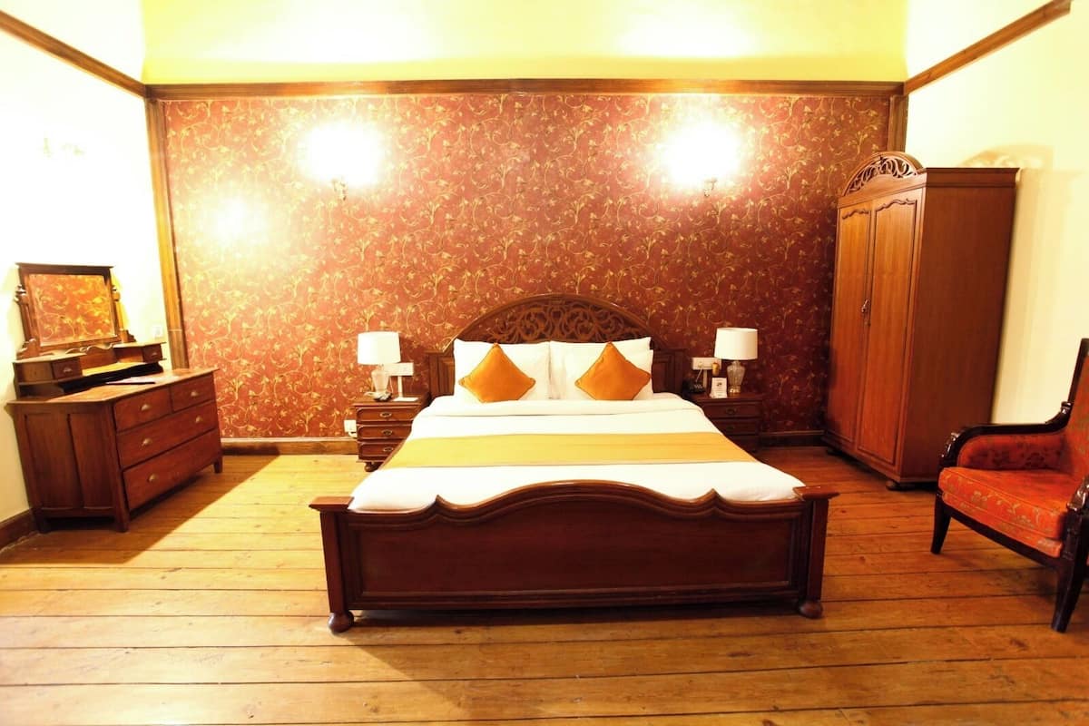 Un dormitorio tradicional con una cama de madera, dos mesitas de noche con lámparas, un aparador, un armario y un sillón rojo.