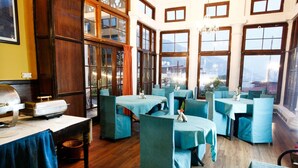Un espace repas avec des tables et des chaises, de grandes fenêtres et un lustre.