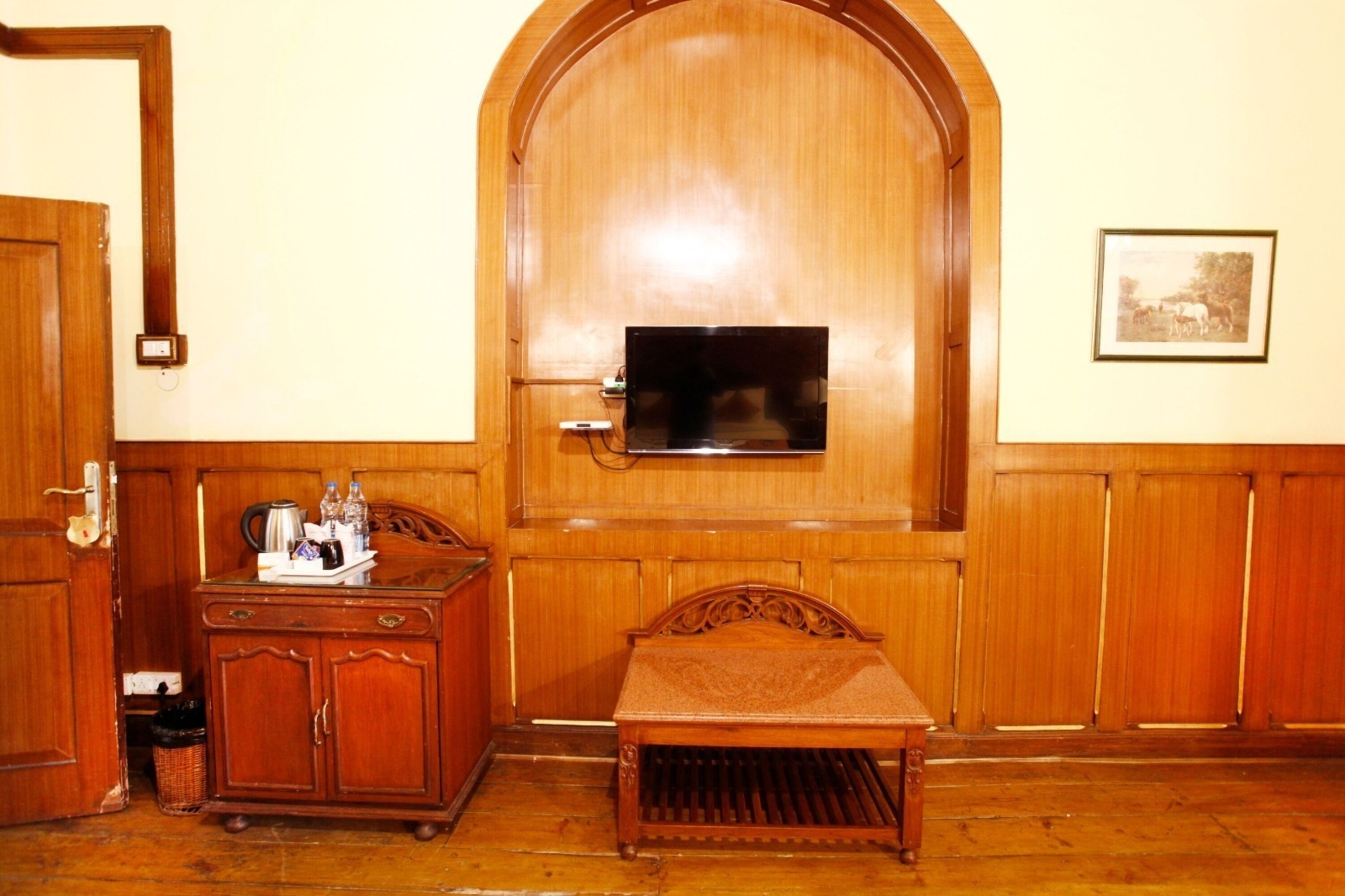 Una habitación con un armario de madera, una mesita pequeña y un televisor montado en una pared de madera.