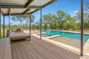 Une terrasse en bois avec une piscine, des chaises longues et un espace salon abrité.