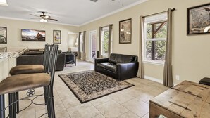 A spacious living room with a black leather sofa, a dining table, and a bar area with stools. - Copper Canyon Hideaway + Free Retro Arcade Fun (Canyon Lake)