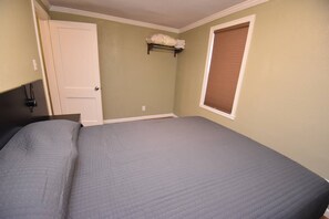 Ein Schlafzimmer mit einem Bett, einer Tür, einem Fenster mit Jalousien und einem Regal mit gefalteten Handtüchern.
