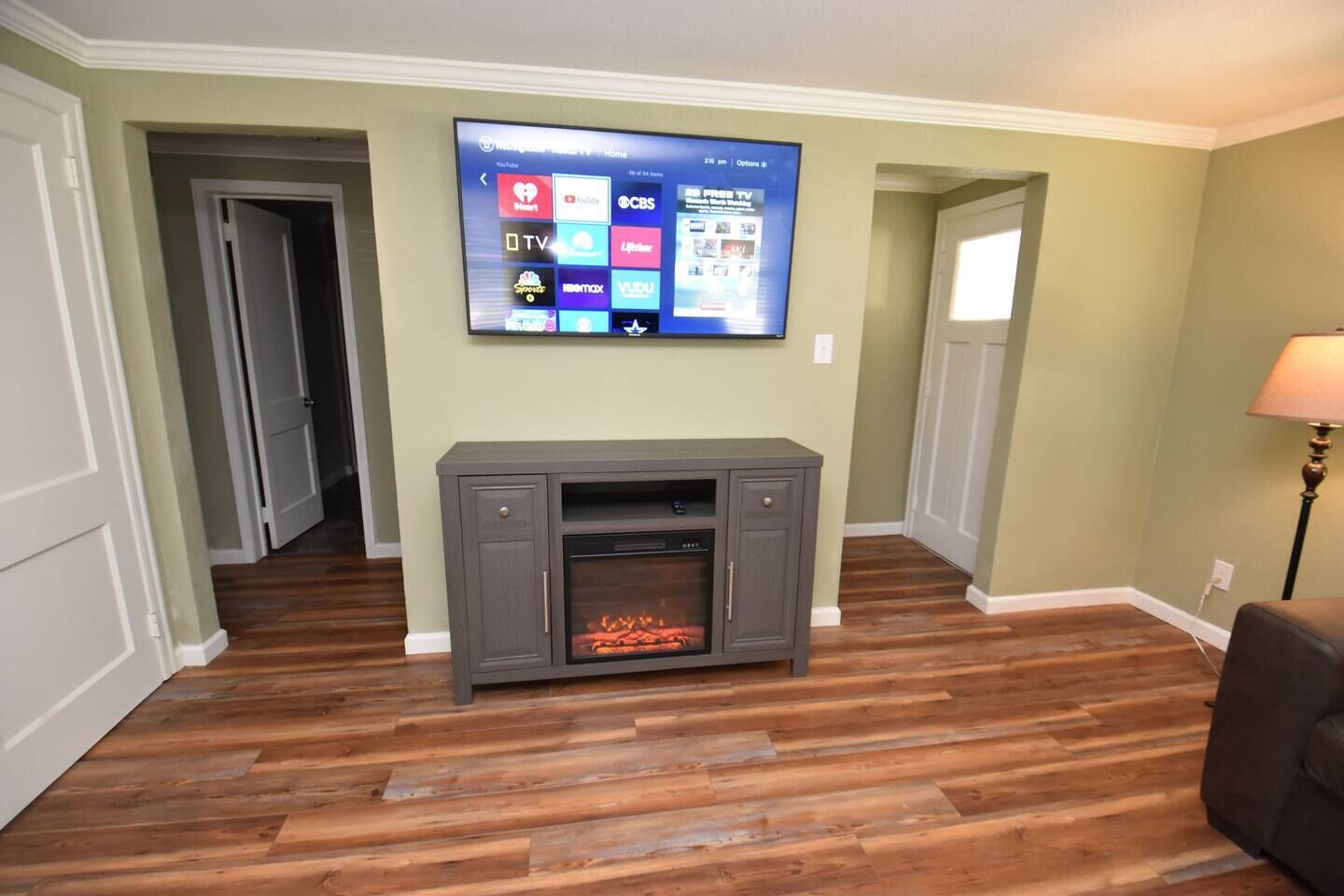 Ein Wohnzimmer mit flachbildfernseher an der Wand, einer grauen Unterhaltungsanlage inklusive Kamin und Holzböden.