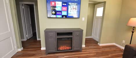Un soggiorno con una TV a schermo piatto montata a parete, un mobile TV grigio con un caminetto sottostante e pavimento in legno.