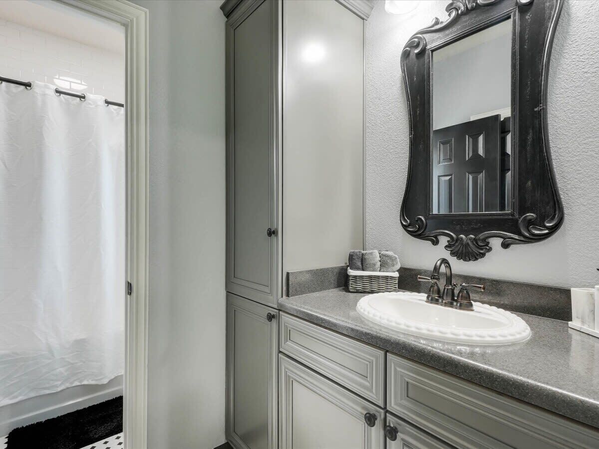 Un baño con un lavamanos blanco, un espejo con un marco ornamentado y una cortina de ducha.