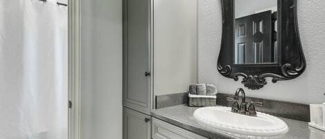 Un baño con un lavamanos blanco, un espejo con un marco ornamentado y una cortina de ducha.