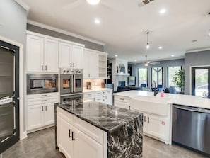 A modern kitchen with white cabinetry, a marble island, and stainless steel appliances.