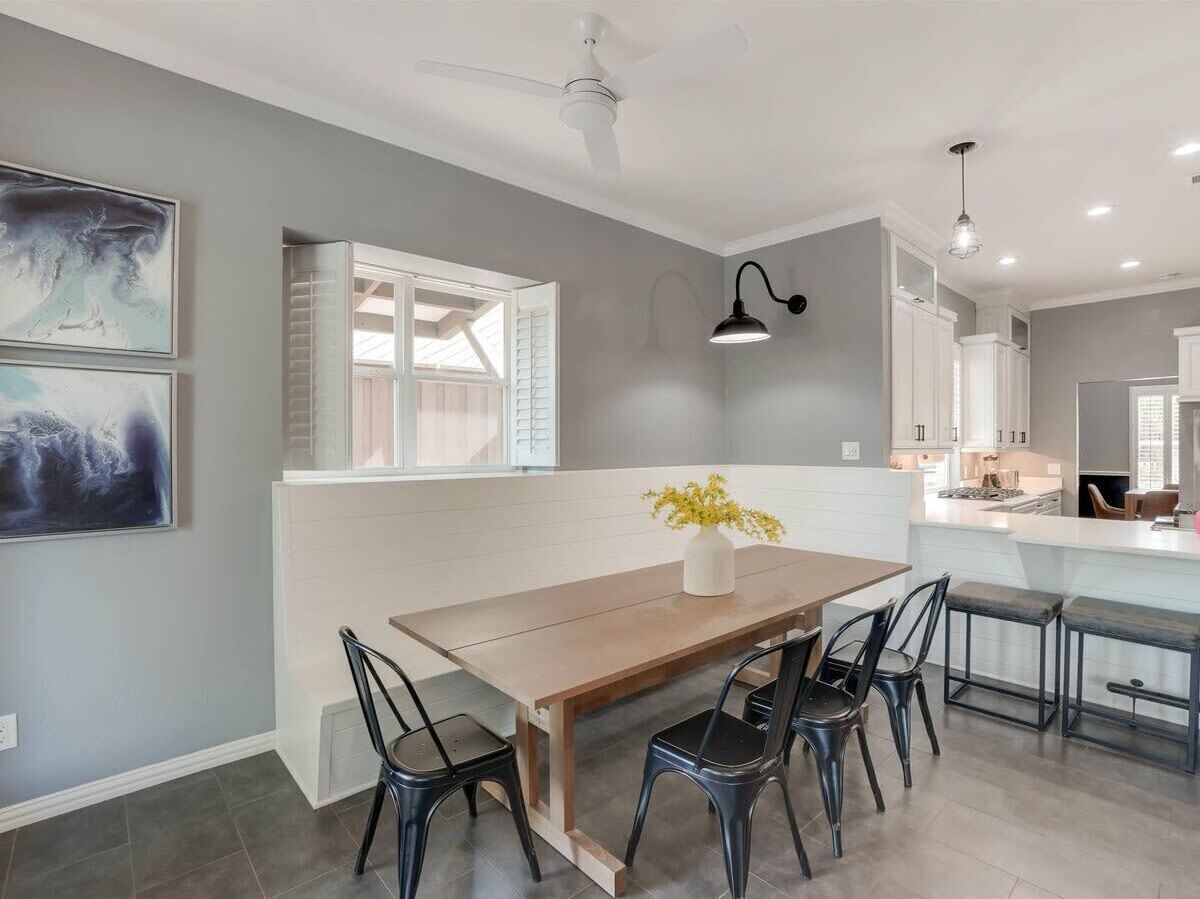 A modern kitchen with a dining area, featuring a wooden table, black chairs, and a vase with yellow flowers.