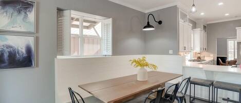 A modern kitchen with a dining area, featuring a wooden table, black chairs, and a vase with yellow flowers.