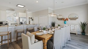 Una cucina moderna con mobili bianchi, un tavolo da pranzo in legno apparecchiato per sei persone e una scala che conduce a un piano superiore.