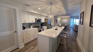 Una cocina moderna con armarios blancos, electrodomésticos de acero inoxidable y una isla central con taburetes de bar.