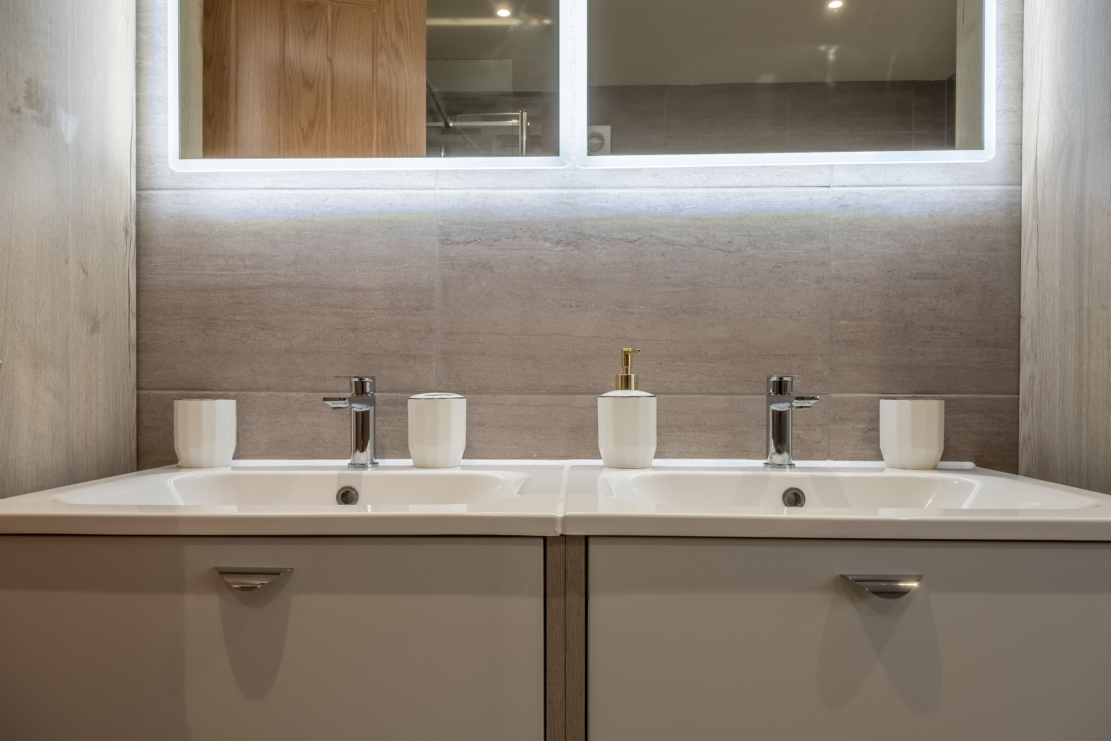 A bathroom with a double sink, two white cups, and a window above.