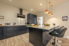 Une cuisine moderne avec des meubles de couleur sombre, un îlot central et des luminaires suspendus.