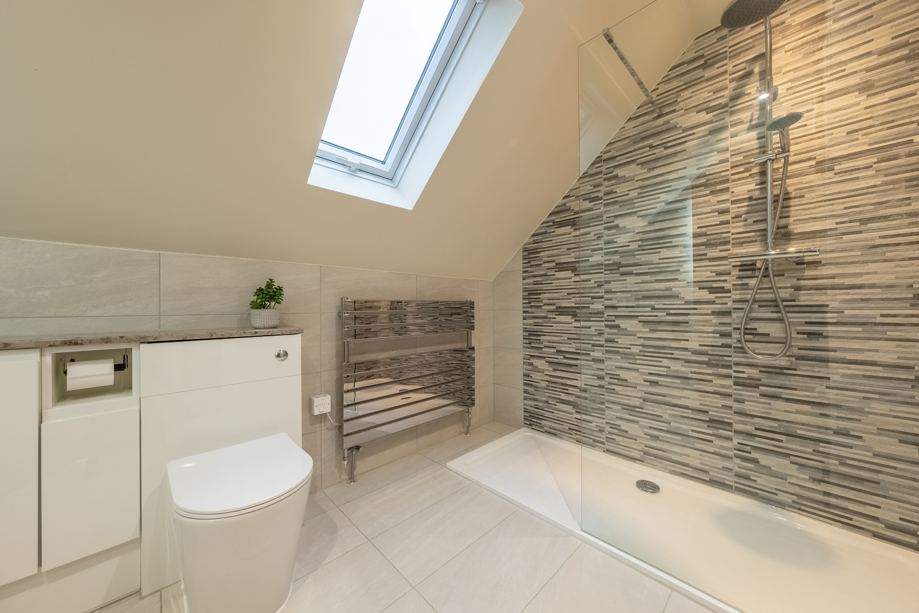 Ein modernes Badezimmer mit Dachfenster, einer gläsernen Duschkabine und einer integrierten Sitzbank.