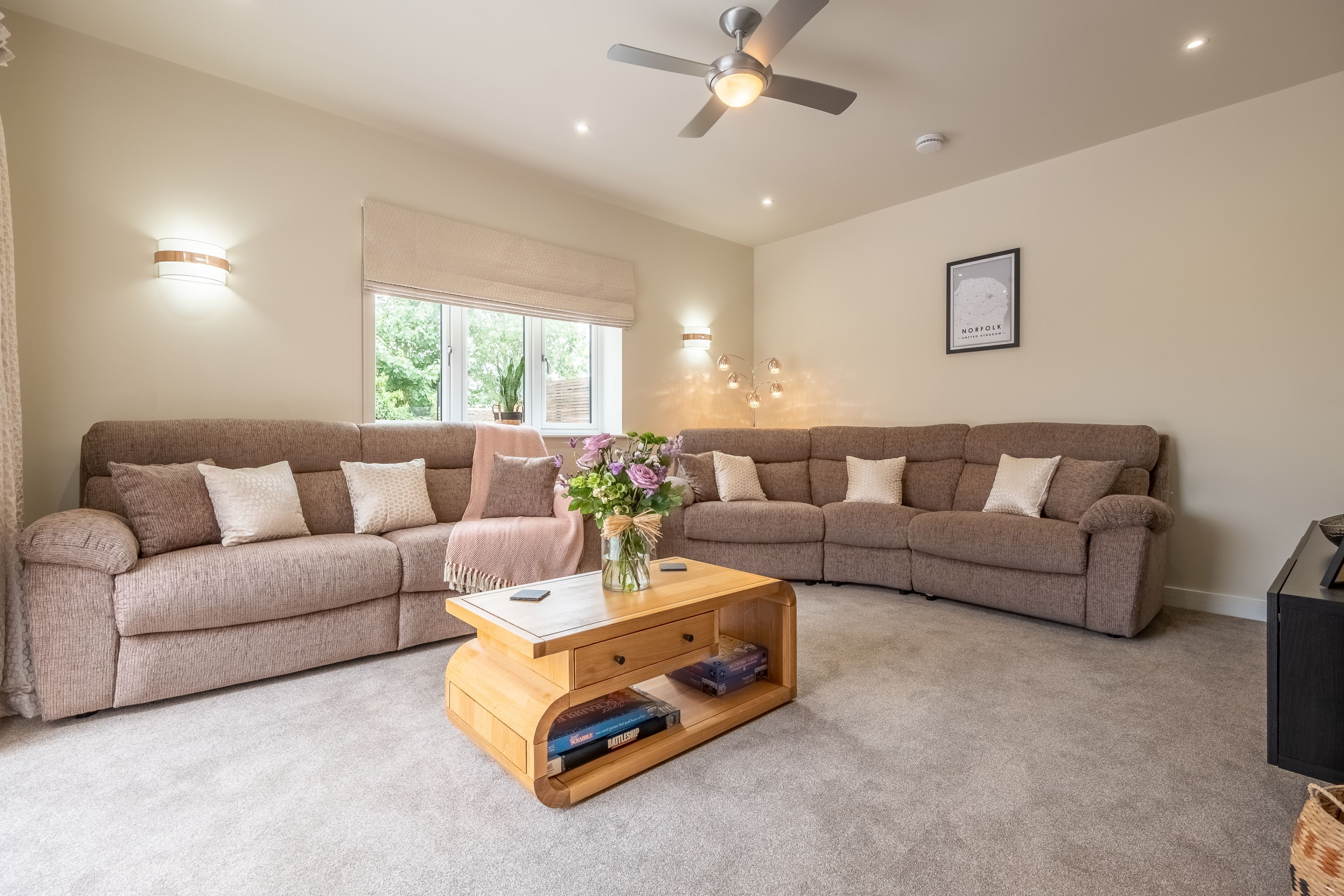 A living room with two beige sofas, a wooden coffee table, and a ceiling fan.