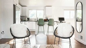 A modern kitchen with white cabinets, a dining area with two chairs, a table, and a large mirror. - Chic Mid-Century Home Near Olde Town Arvada (Arvada)