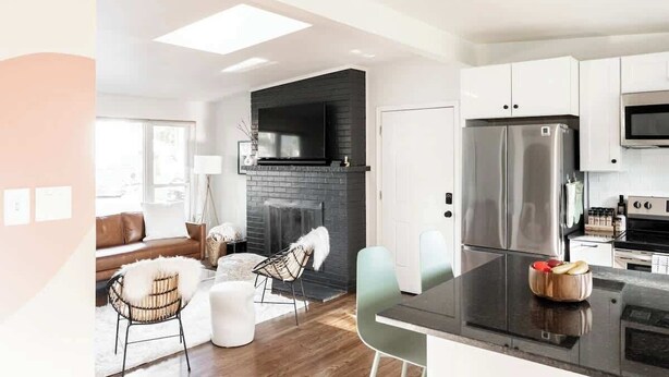 A modern kitchen with stainless steel appliances, a black brick fireplace, and a dining area with a white sofa and chairs. - Chic Mid-Century Home Near Olde Town Arvada (Arvada)
