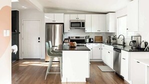 A modern kitchen with white cabinets, stainless steel appliances, and a central island. - Chic Mid-Century Home Near Olde Town Arvada (Arvada)