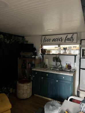 A compact kitchen with a built-in sink, a countertop with various kitchen items, and a sign above stating 'love never fails'.