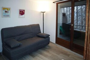 A room with a dark grey sofa, a floor lamp, and a sliding glass door leading to an outdoor area with a green chair. - 300m from ski slopes, 4th floor, view valley, balcony, tv, 22m², Les Orres (Les Orres)