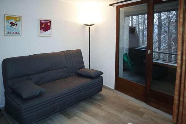 A room with a dark grey sofa, a floor lamp, and a sliding glass door leading to an outdoor area with a green chair.