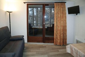 A room with a sofa, a table, a TV, and a sliding glass door leading to a balcony.